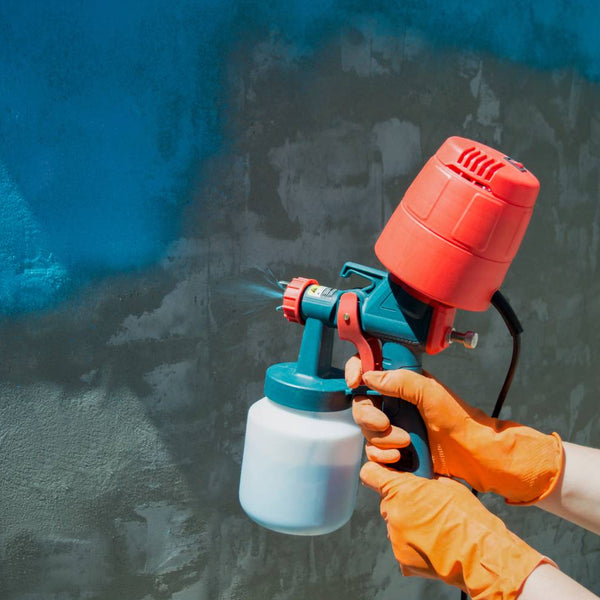 Hands covered with orange gloves using an orange paint sprayer