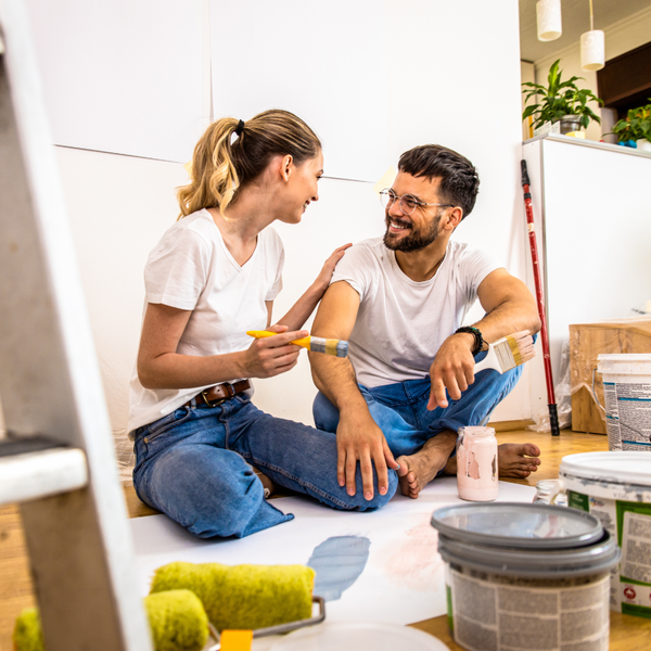 A couple sitting together on the floor in their home with buckets of interior paint