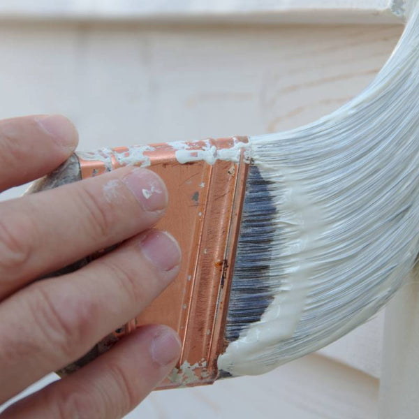 Person holding a brush covered in primer, brushing it against a wall