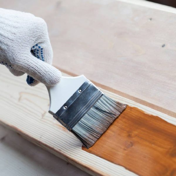 Gloved hand holding a brush applying stain to a wooden board at Hoover Paint near Murfreesboro, TN