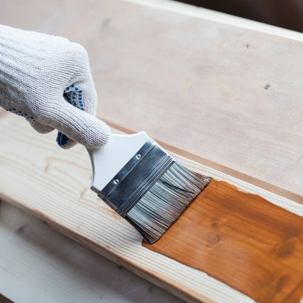 Gloved hand holding a brush applying stain to a wooden board at Hoover Paint near Murfreesboro, TN