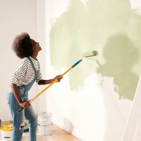 A person using a paint roller to paint a wall green