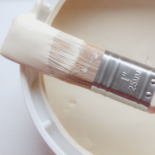  Open paint can with a white eggshell color and a paint brush lying across the opening