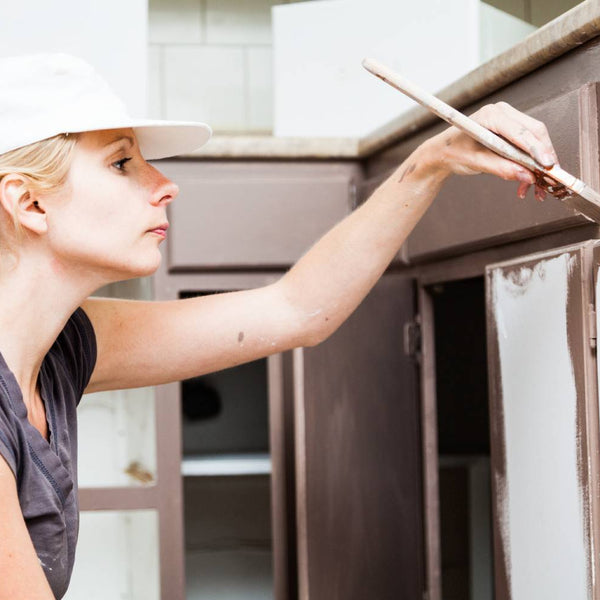Woman painting kitchen cabinets with brown Benjamin Moore Advance Paint