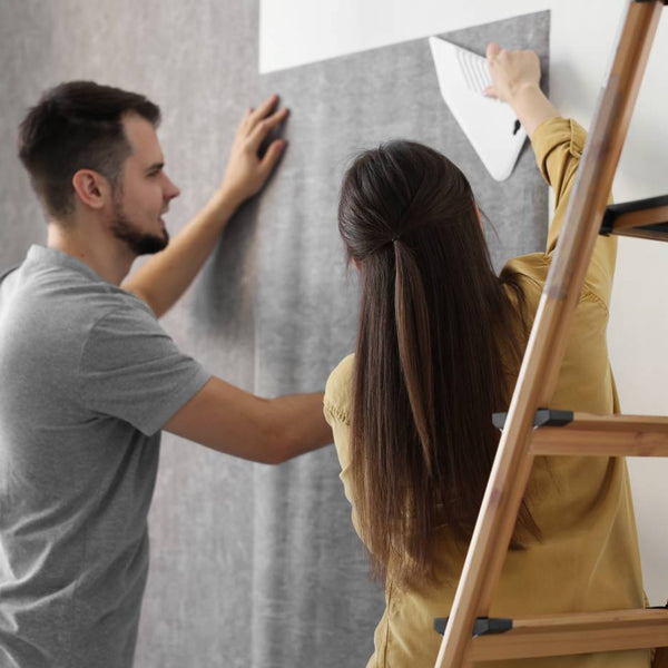 A couple working together to hang their stylish and textured gray home interior wallpaper